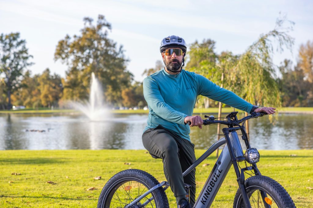 A man wearing a helmet rides a bicycle in a scenic park near a fountain.